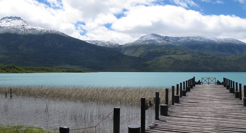 A stock stretches out over a blue body of water. Beyond the water, there are mountains. 